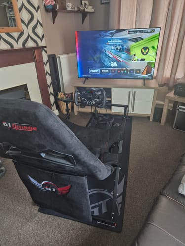 Customer's black SPRINT Folding Cockpit set up in a living room, facing a TV with a racing game displayed.