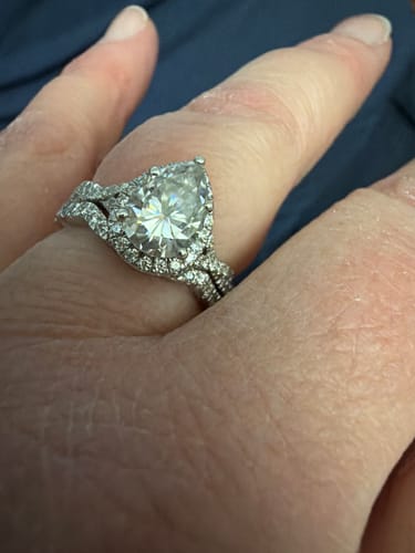 Customer showing their custom pear-shaped moissanite ring set with a matching curved, stone-accented band.