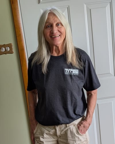 Reviewer smiling and wearing the front of the dark gray Hard Days t-shirt indoors.