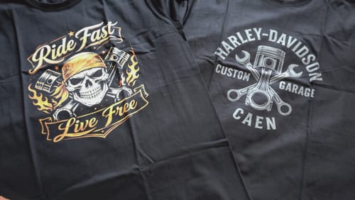 Client montrant deux t-shirts noirs à motifs, dont le T-shirt Custom Garage avec un piston et un autre avec une tête de mort.