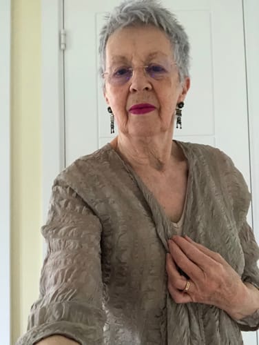 A reviewer tries on the open beige textured silk jacket, holding one lapel.