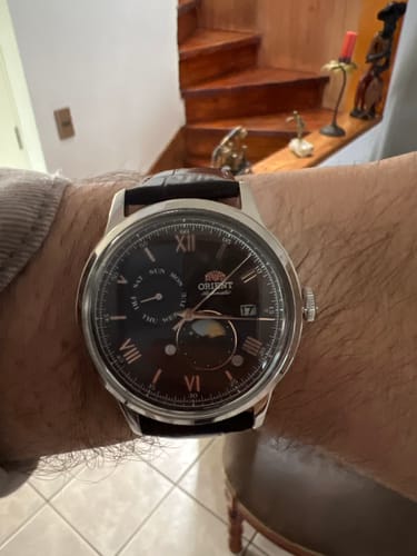 Un cliente muestra en su muñeca el reloj Orient Bambino Sun & Moon, destacando su esfera oscura y caja plateada.