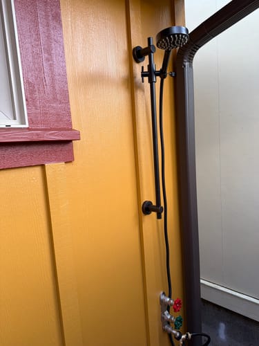 Customer's black slide bar with handheld shower head set installed on a yellow wall.