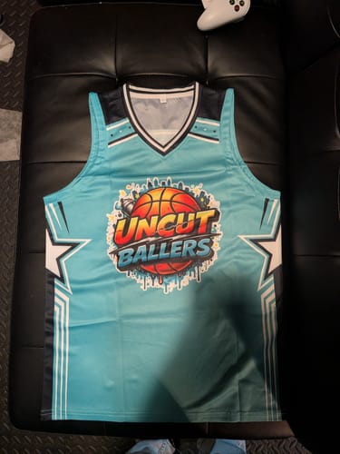 Customer's custom aqua basketball jersey with a graffiti-style 'Uncut Ballers' graphic laid flat on a couch.