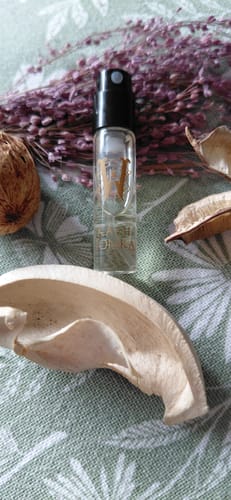 Reviewer's sample vial of Kami Tonka perfume, displayed with dried purple flowers and other botanicals on a green cloth.