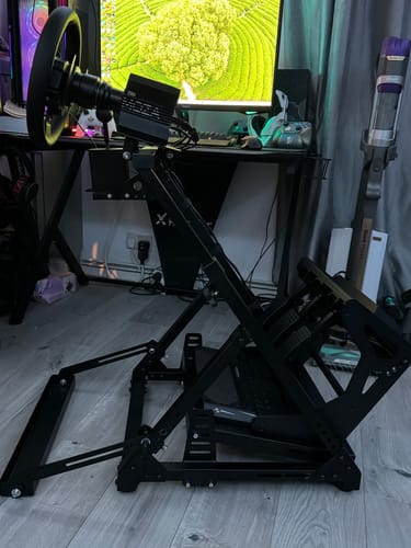 Customer's black DD-X Wheel Stand set up on a wooden floor, showing a modification to the pedal tray.
