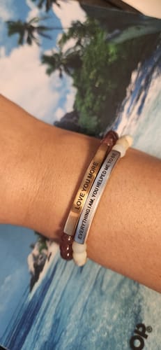 Close-up of a customer's wrist wearing two stacked bracelets, including the 'EVERYTHING I AM YOU HELPED ME TO BE' bracelet.