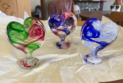 Reviewer's three colorful Glass Hearts with Cremains sitting on a white cloth-covered table.
