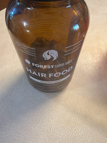 Close-up of a customer's brown bottle of Forest Super Foods Hair Food on a light-colored table.
