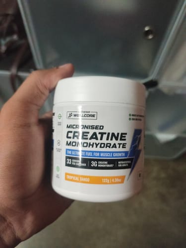 Customer holds a white tub of Wellcore Micronised Creatine Monohydrate in the Tropical Tango flavor.