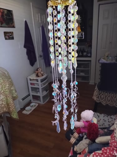 Reviewer's completed sun catcher from the craft kit hanging indoors, showing long strands of iridescent crystals.