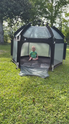 Reviewer's baby sits inside the large black Pop 'N Go Playpen on a lawn.