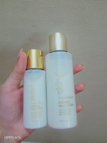 Customer's hand holding a large and a small bottle of the DREAM GLAZE Peptide Milk Toner against a neutral background.