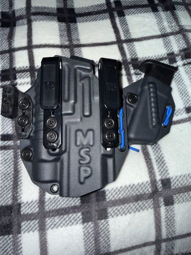Customer's black MSP PRO SERIES FLX holster with attached magazine carrier, viewed from the front on a plaid surface.