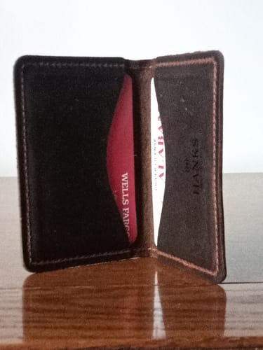 Customer's dark leather Tupper Bifold Card Holder standing open with cards in both pockets.