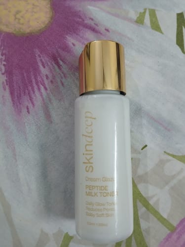 Customer's white bottle of DREAM GLAZE Peptide Milk Toner with its shiny gold cap, seen up close.
