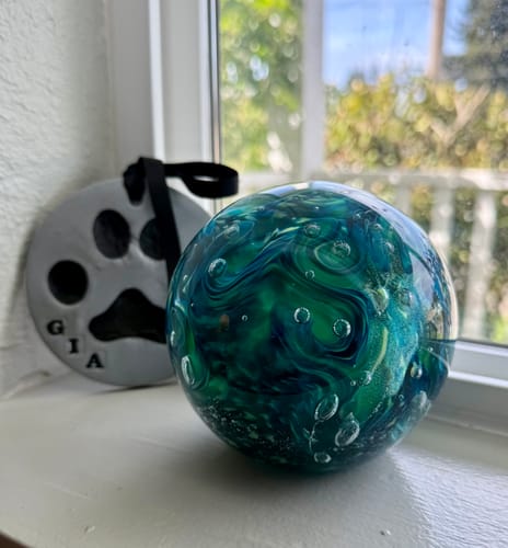 Reviewer's blue and green Dichroic Splash Orb, a pet memorial, on a windowsill.