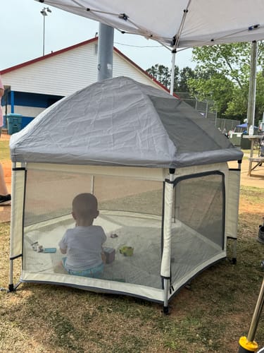 Customer's Pop 'N Go Playpen set up at a ballfield, with a child sitting inside under the shade cover.