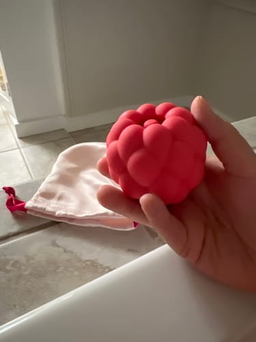 Customer holding the red Berri Tapping Massager in their palm, with the storage bag visible on the edge of a bathtub.