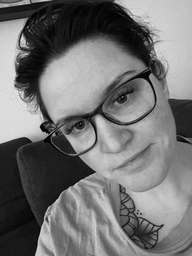 Schwarz-Weiß-Aufnahme einer Kundin mit Brille, die ihre langen AYLASHES Wimpernextensions zeigt.