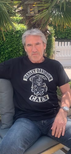 Client portant le T-shirt noir Faucheuse HC avec un grand imprimé, assis en extérieur.
