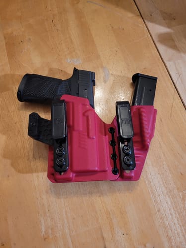 Customer's pink AXIS ELITE holster with a handgun and magazine secured inside, shown on a wooden table.