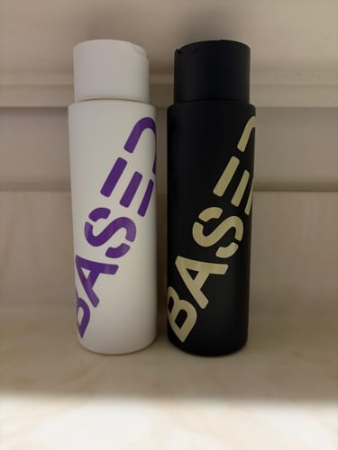 Customer's Shower Duo shampoo and conditioner bottles, one white and one black, standing side-by-side on a shelf.