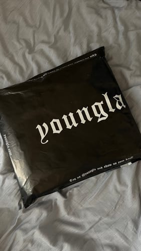 Customer's black Youngla shipping package resting on a grey bedspread.