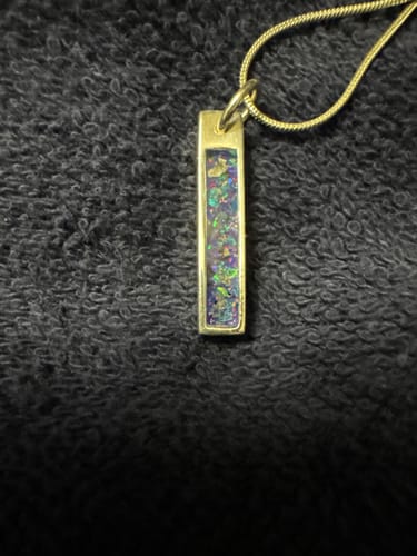 Reviewer's gold-plated Opal Bar Pendant showing a turquoise, blue, and magenta opal inlay against a dark textured background.