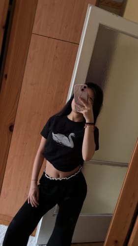 Reviewer taking a mirror selfie while wearing the black swan song baby tee with black pants.