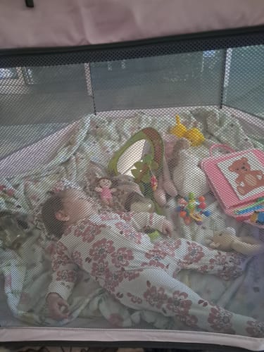 A customer's baby resting inside a pink Pop 'N Go Playpen with toys, viewed through the mesh siding.