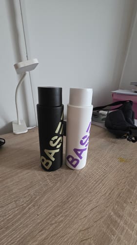 Customer's Shower Duo shampoo and conditioner bottles, one black and one white, sitting on a wooden desk.