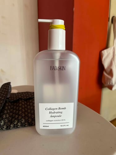 Reviewer's bottle of Bad Skin Collagen Bomb Hydrating Ampoule with a yellow band wrapped around the pump to control dispensing.