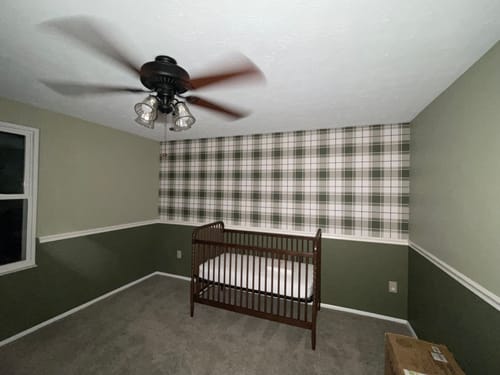 Customer's green plaid Baker Wallpaper installed as an accent wall in a nursery room above a crib.
