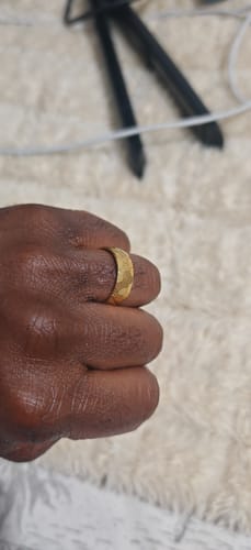 A reviewer's hand wearing the textured gold Draxor ring against a white background.