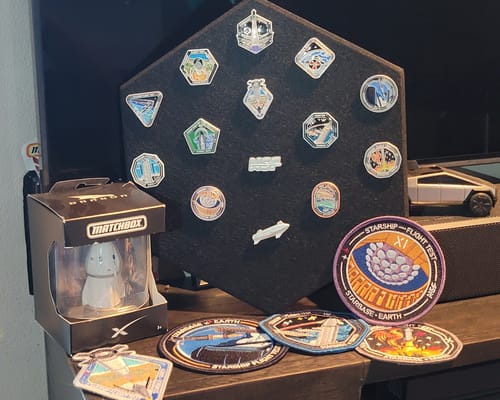 Customer's black hexagonal Starship Pin Display Mount with pins, displayed on a shelf with other space-themed collectibles.
