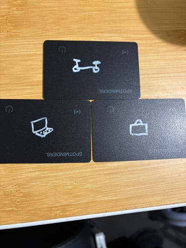 Customer's three black SPOTMINDERS Tracking Cards, each personalized with a white drawing of a laptop, scooter, and luggage.