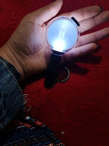Reviewer holding the lit BTS Official Light Stick Keyring SE in their hand against a red background.
