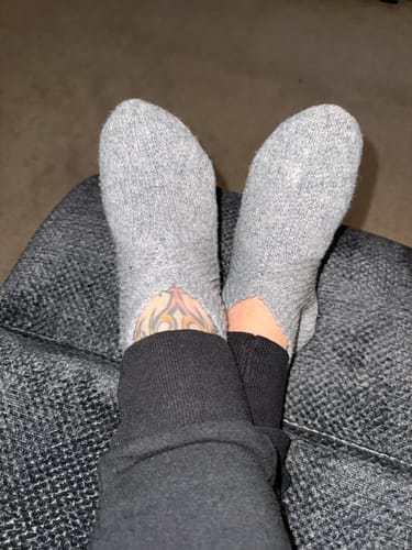 Reviewer relaxing with feet up, wearing the soft grey Gripper Slippers on a dark grey chair.
