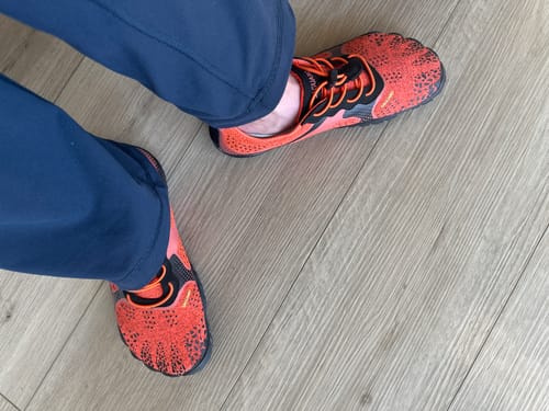 Customer wearing bright orange and black Fast Ⅰ - Barefoot Shoes indoors on a light wood floor.