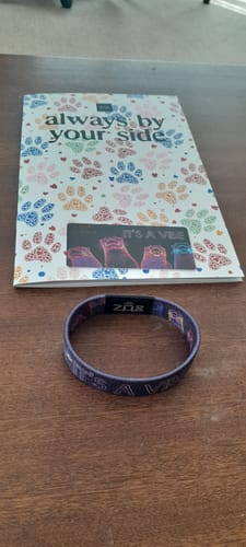 Customer's It's A Vibe Bracelet on a wooden table next to its accompanying booklet and collector's card.