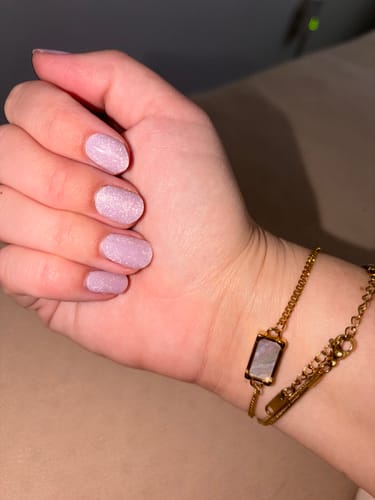 Hand einer Kundin mit manikürten Nägeln, die die schimmernden rosa UV Gel Nail Wraps 'Glazed Donut Cateye' trägt