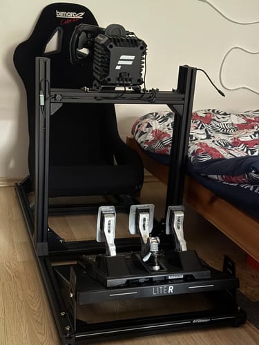 Customer's fully assembled black PRIME Lite-R Cockpit with a racing seat, wheel, and pedals set up indoors.