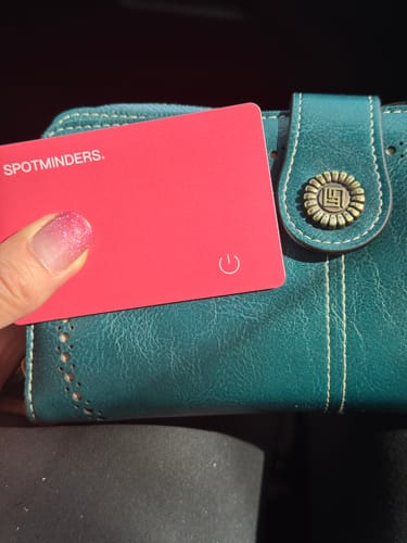 Customer holding the pink SPOTMINDERS Tracking Card next to a teal wallet.