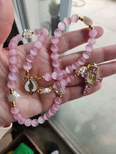 Reviewer's hand holding the soft pink Cat's Eye Rosary, showing its luminous beads and rose accents.