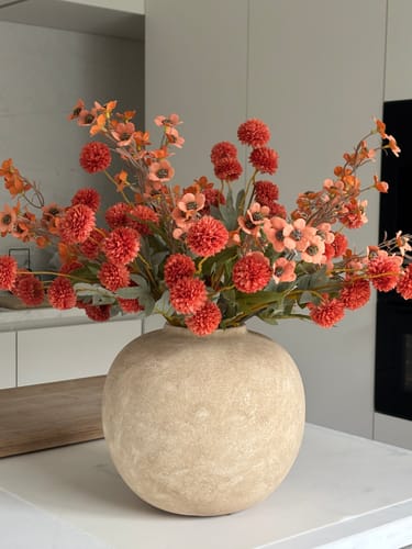 Recensent toont het Wax arrangement - Terracotta in een ronde, beige vaas op een aanrecht in de keuken.