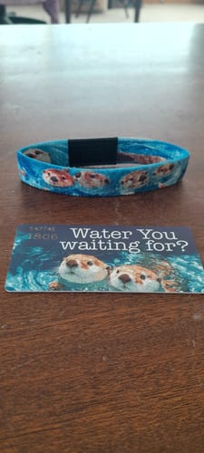 Reviewer's blue, otter-print 'Water You Waiting For?' bracelet displayed on a table next to its matching themed card.