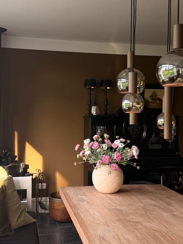 Klant toont het Ranonkel Arrangement in een lichte vaas op een houten eettafel.