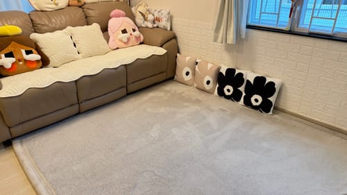 Customer's large grey Momomi® Mat placed on the floor of a living room in front of a brown sofa.