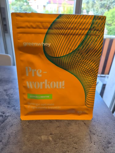 Client présentant le sachet orange de Pre-Workout saveur Citron & Menthe sur une table.